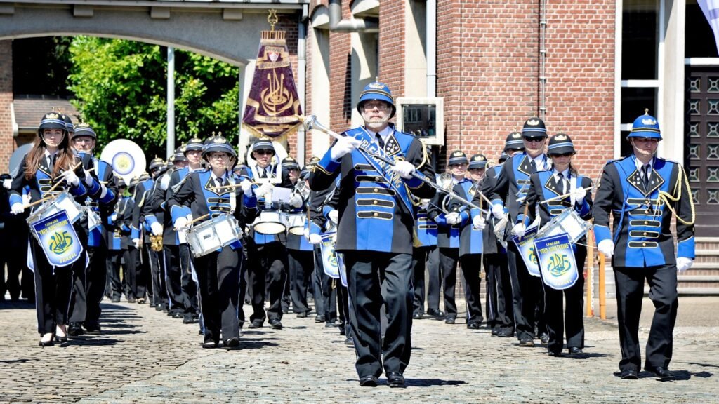 Het fanfarekorps in blauw uniform marcheert over de kasseien, met de tamboer-majoor vooraan
