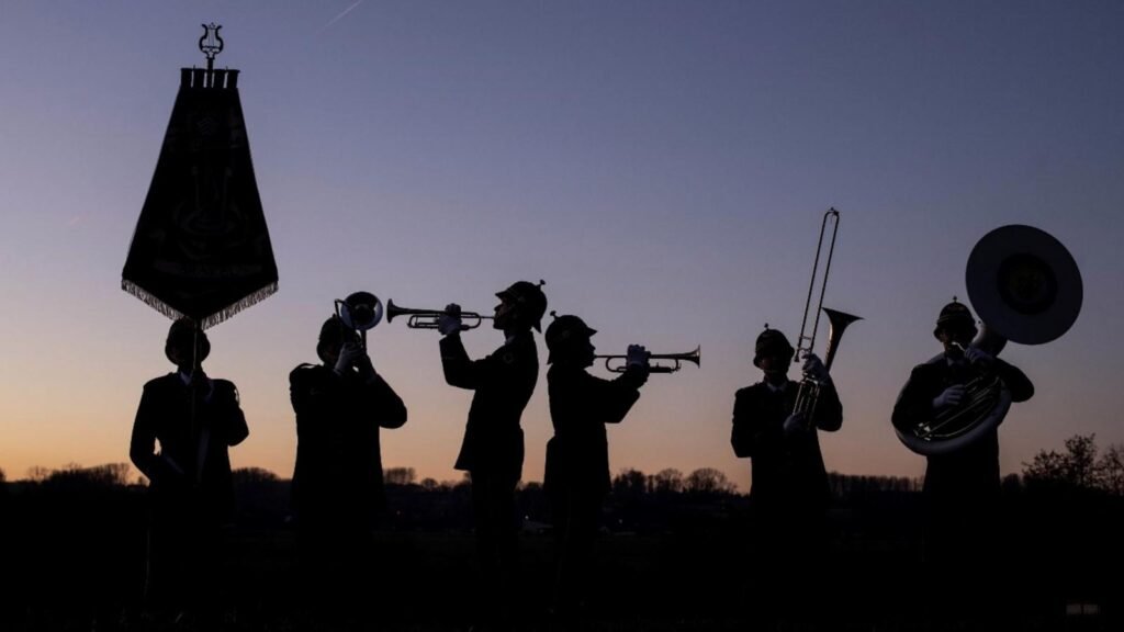 Silhouetten van muzikanten van het korps tegen de avondlucht, met het vaandel