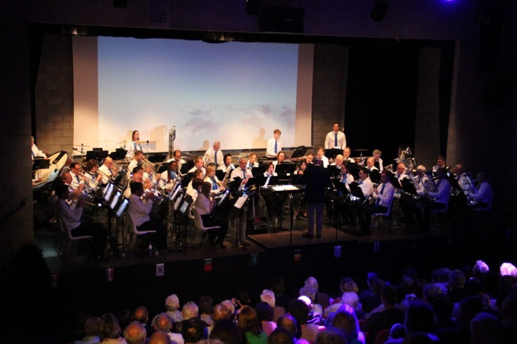 Music For Friends op het podium, met de dirigent vooraan en publiek in de zaal